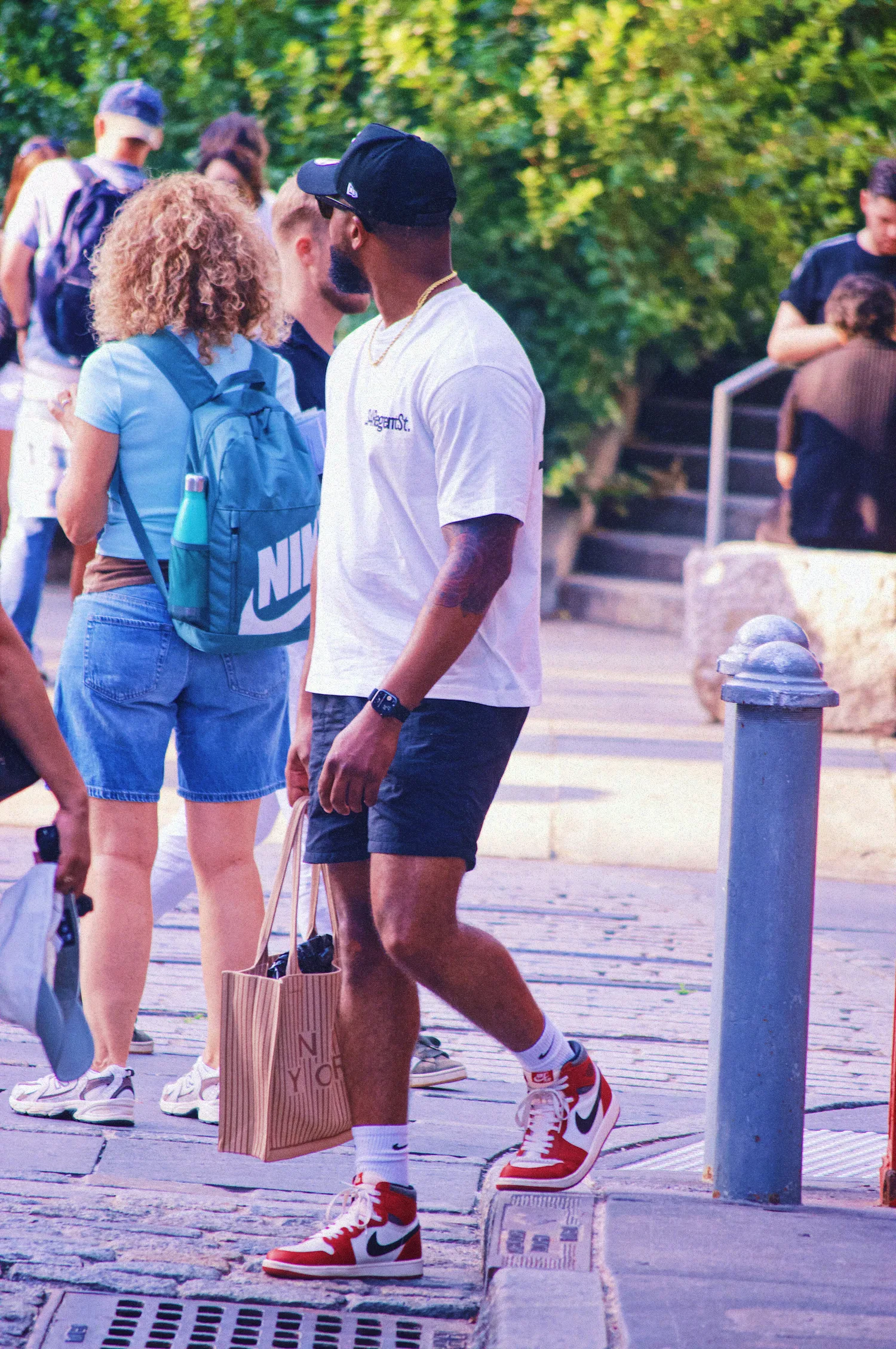 Keon NaVarr walking along a tree-lined city street carrying a shopping bag