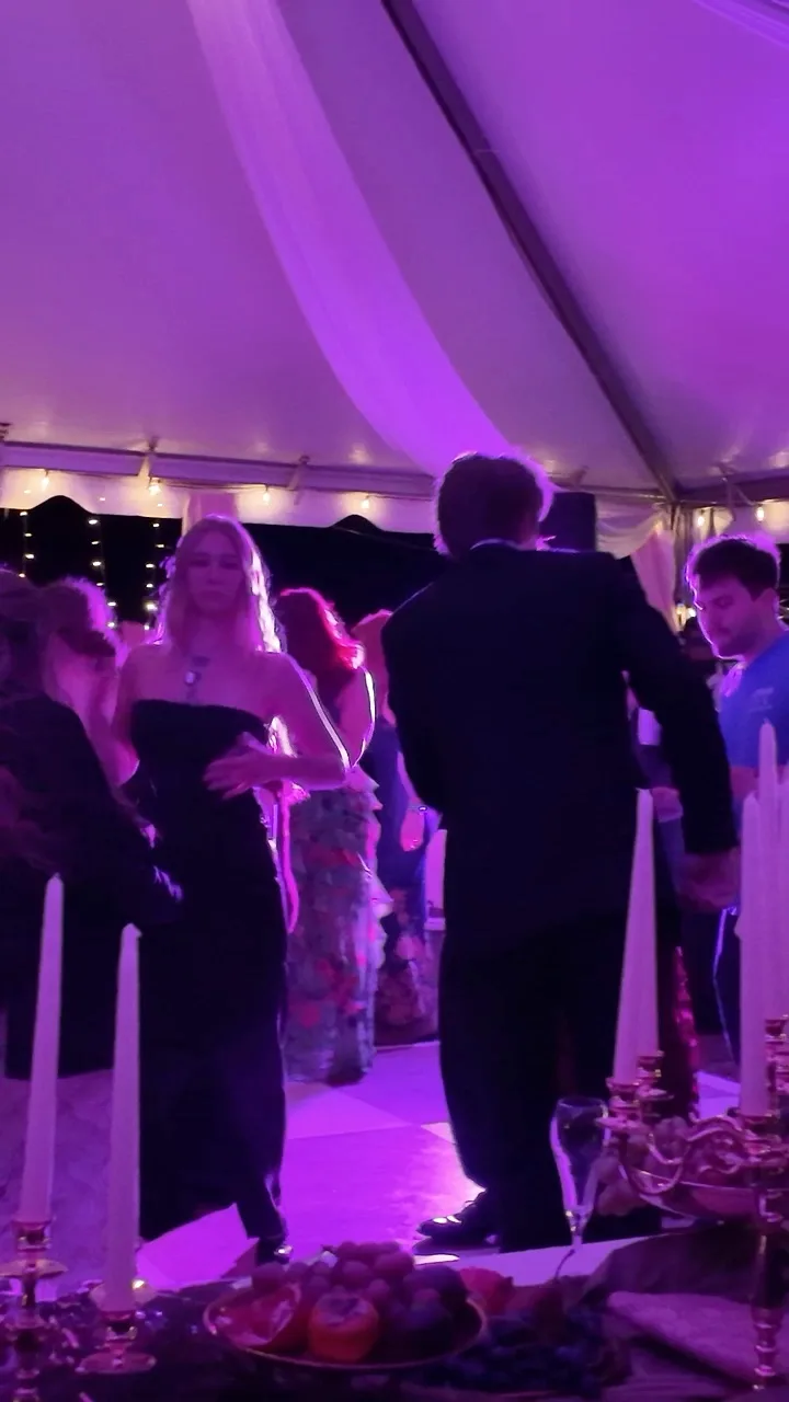 Wedding guests dancing beneath a tent illuminated with purple light