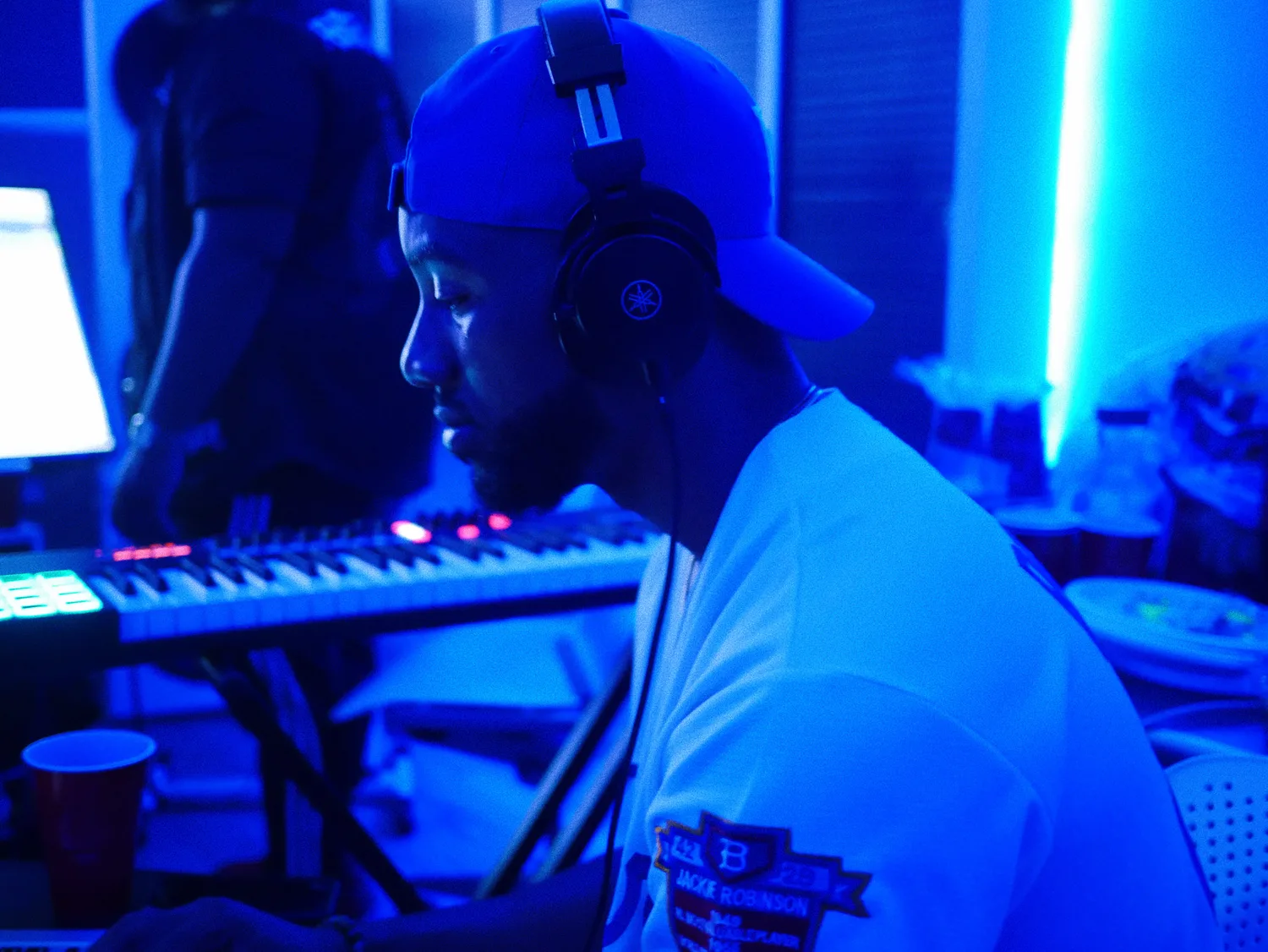 Keon NaVarr wearing headphones at a keyboard in a blue-lit studio